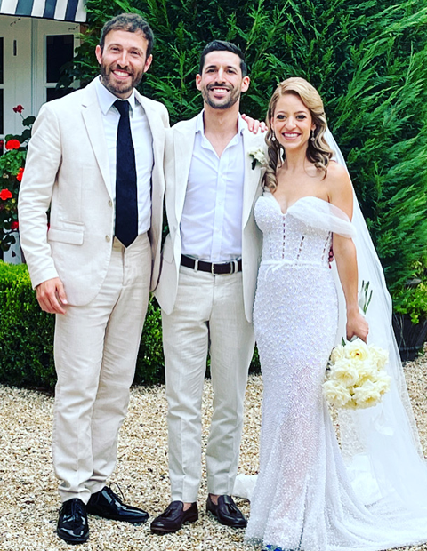 Rabbi Yossi standing with a bride and groom in a garden, all three smiling at the camera