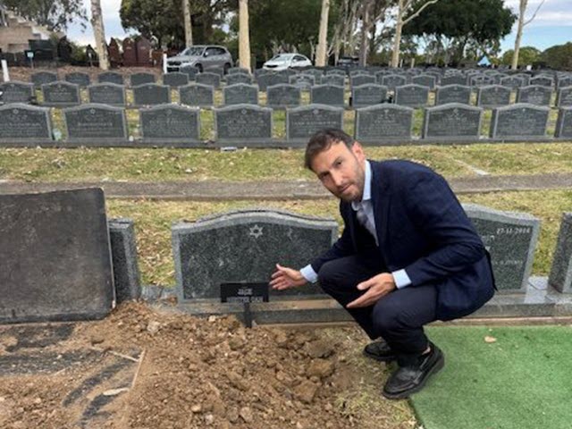 Rabbi Yossi crouching beside a freshly prepared grave, speaking with family at a Jewish cemetery.