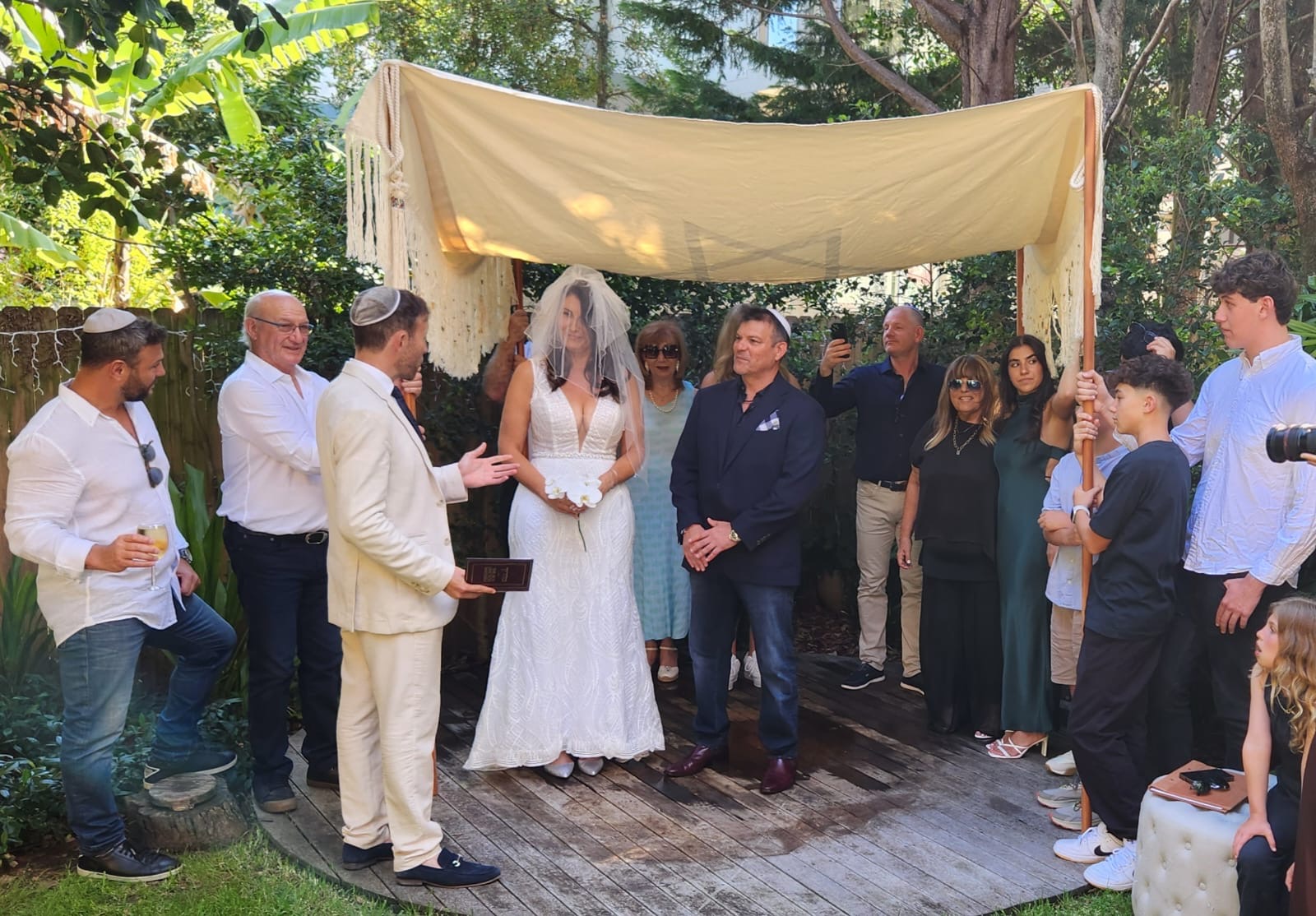 Rabbi Yossi officiating beneath a chuppah as the bride and groom stand together with family and guests